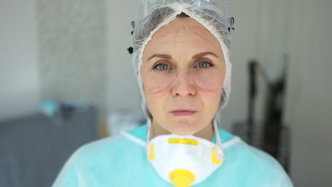Close portrait of a tired doctor. Female doctor during a coronavirus pandemic covid-19 takes off glasses and a protective mask, face marks are visible from the mask, red spots