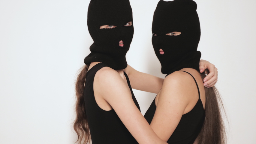 Two beautiful sexy women in black swimwear bathing suit. Models wearing bandit balaclava mask.Hot girls posing near white wall in studio.Seductive female in nice lingerie.Crime and violence