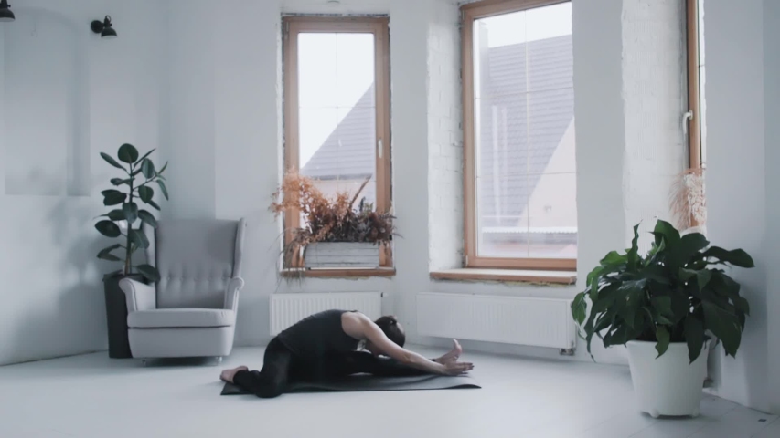 Cameraman shooting fit young brunette girl in sportswear stretching, leaning forward on mat at home. Videographer shoots sporty female doing exercizes, backstage of making video on healthy lifestyle