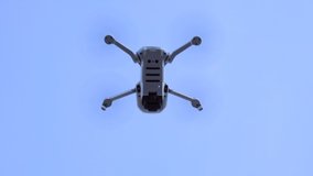 Gray drone flying in above, with rotating blades. Hanging in the air for sometimes, after go up and away. Outdoors, clear blue sky background.