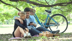 Young couple in love sitting on mat  using smartphone to video call on picnic in the park. dating, romance outdoors 