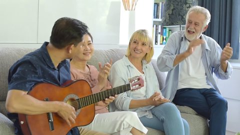 Slow motion, Group of positive seniors European and Asia are singing with playing a guitar at retirement home. Retired people are playing music which fun to enjoying and smiling felling happy.