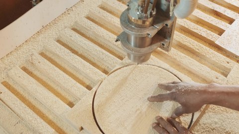 Cutting wood with a CNC milling machines. The carpenter holds the part with his hand