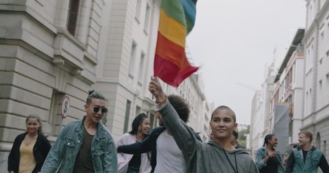 Young woman waving a rainbow flag in a gay parade. Group of people participating in gay pride march.

