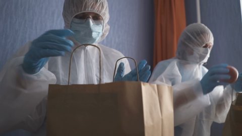 Volunteer in protective suits pack products. Food delivery services during coronavirus pandemic for working from home and social distancing. Shopping online. : vidéo de stock