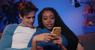 Millennial couple talking and looking at phone screen.Young woman with dreadlocks making surprised facial expression while using smartphone and spending time with boyfriend.