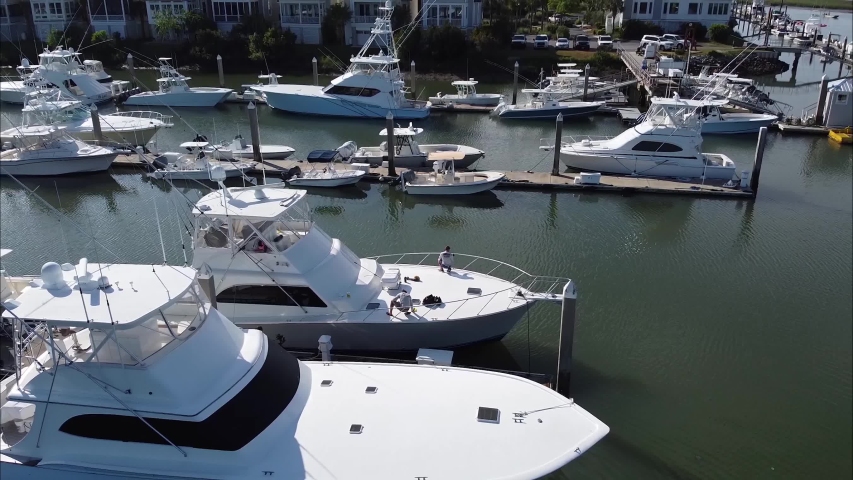 Aerial view flying People on deck serve the yacht before sailing. Deck polishing boats docked in harbor at sunset. Many different yachts, catamarans moored to piers. Drone shot