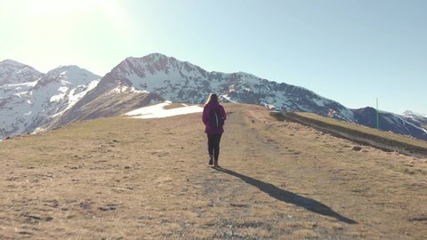 DRONE FOOTAGE - Young woman walking in mountains hiking trail alone. Snow and mountain peaks in the french Pyrenees near the Luchon Superbagnères Ski Resort in Saint-Aventin, France.