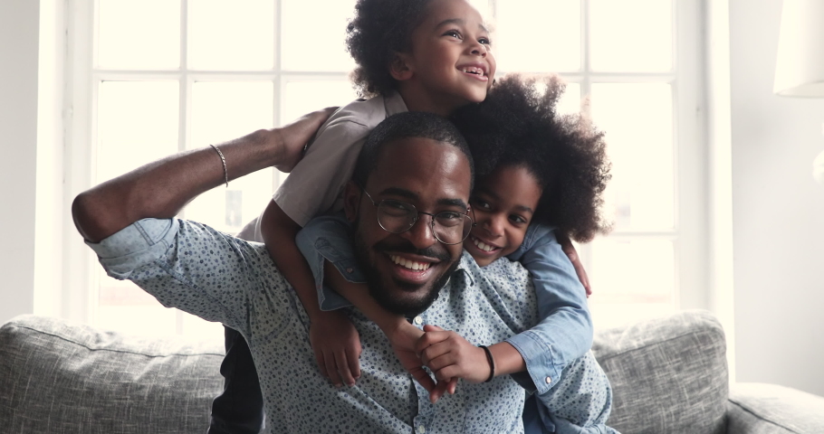 Head shot happy young african american man playing with little cute children siblings indoors. Overjoyed small brother and sister having fun, embracing laughing father, spending leisure time at home. Royalty-Free Stock Footage #1051777252