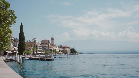 Amazing famous view on Garda lake from Gardone Riviera. Lakefront of the famous touristic resort city in a sunny spring day. Traditional Italian architecture, marina, splashing water. Long shot