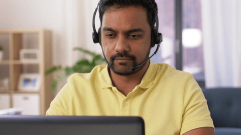 remote job, technology and people concept - indian man with headset and laptop computer having video conference at home office