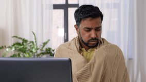 healthcare, technology and people concept - sick indian man in blanket with sore throat having video call on laptop computer at home