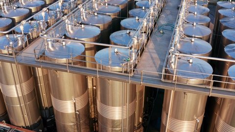 Rows of tall stainless steel tanks connected with pipes. Shiny silos in a chemical industry plant. Metal containers with hazardous chemicals. Aerial footage.