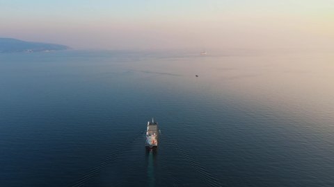 Aerial view following the ultra large cargo ship at sea leaves port at sunset. Top down backside drone footage of tanker. Concept of transport logistics, maritime.