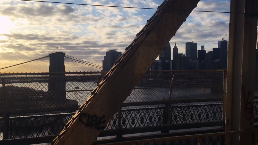 Glimpse of Manhattan and the Brooklyn Bridge at sunset interspersed with the passage of metal beams from the subway window while crossing the East River on a bridge in the direction of Downtown Royalty-Free Stock Footage #1051802389