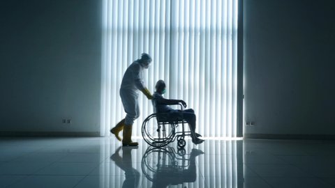 JAKARTA - Indonesia. April 28, 2020: Coronavirus concept. Silhouette of old man sitting on wheelchair and pushed by his doctor near the window during quarantine at home. Shot in 4k resolution