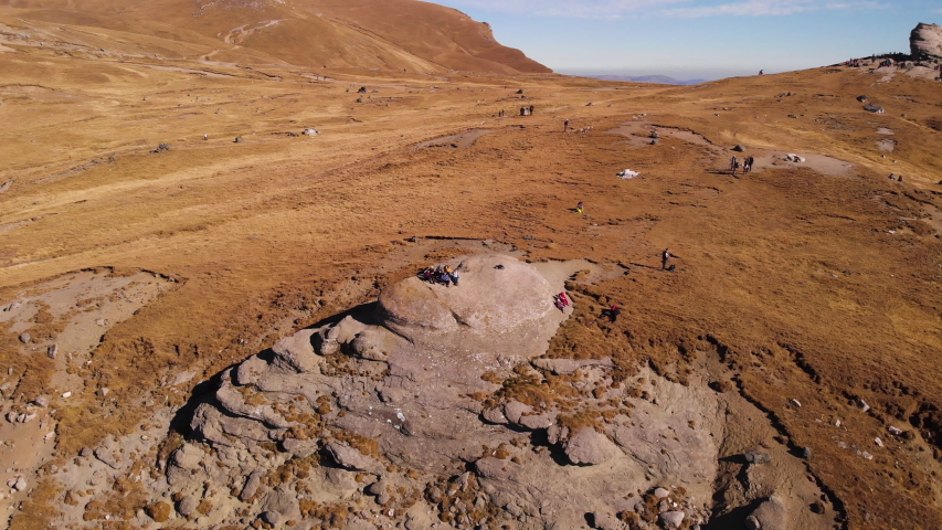 Aerial 4k view of tourists sitting on a big rock on the Bucegi mountain plateau with Sphinx monument in the background in Transylvania, Romania, Europe, orbiting left shot