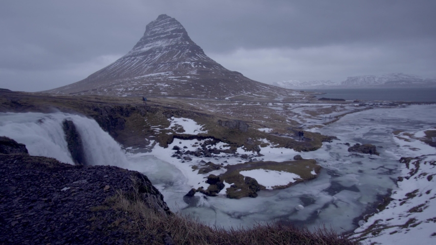 A vast icy landscape. A waterfall and frozen river foregrounds a moody mountain. Tripod. Fixed Focus. Wide Field of View. Landscape. Iceland. 23.976 FPS.