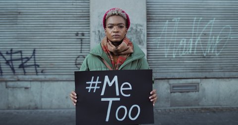 Lviv, Ukraine - November 27, 2019: Time lapse of young woman with MeToo banner standing at street. Young girl supporting me too movement while crowd of people are passing by.