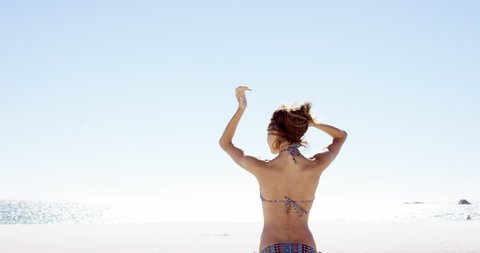 beautiful young woman tying up hair on windy day on tropical beach slow motion