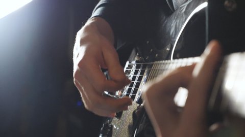 Hands of guy performing solo of rock music. Close up arms of musician playing on electric guitar. Male fingers of guitarist strumming the strings. Adult man composing a new melody. Slow motion