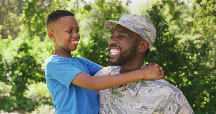 Mixed race man wearing a military uniform, returning home, standing in a garden, embracing his son and smiling, in slow motion