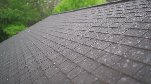 Slow Motion of hail storm hitting roof shingles causing roof damage in summer thunderstorm of severe weather.