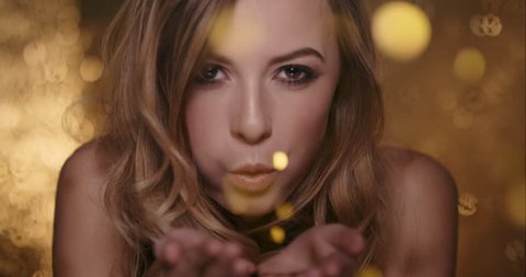 Sexy woman with beautiful face blowing gold glitter in front of shiny shimmer curtain background slow motion shot in 6K Red Epic Dragon