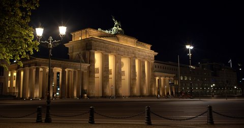 Cinematic wide angle shot from behind-left side of Brandenburger with light and tree in 4k footage at night. Berlin is almost empty during coronavirus time and without tourist in spring April 2020 