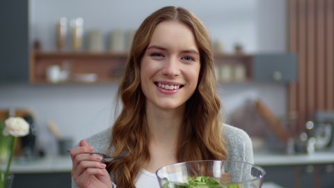 Portrait of smiling woman eating fresh salad at home kitchen. Beautiful girl tasting vegetarian food at modern apartment. Closeup young woman keeping tomato on fork indoors.