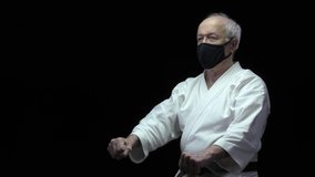 On a black background, an old athlete is training formal karate exercises in self-isolation