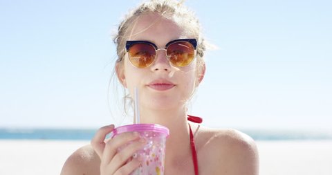 Close up portrait of beautiful young teenage girl drinking water from pink plastic cup on tropical beach slow motion