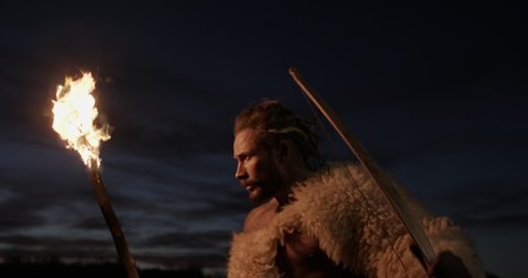 Man dressed in sheepskins walking at night, Man dressed in sheepskins walking at night outdoors in the wilderness by the light of a flaming branch as a torch