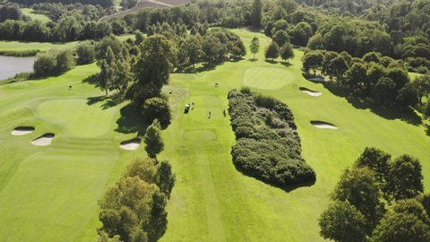 Aerial view of golf course in Ireland on sunny day, aerial drone fly up showcase the golfers on teeing grounds ready to play with golf cart, big fancy golf course