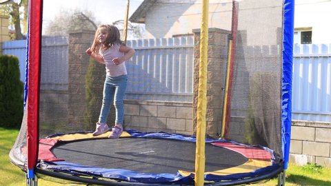 Little girl jumping on a big trampoline in the yard of the house. A child in isolation in the yard of his house plays on the lawn.