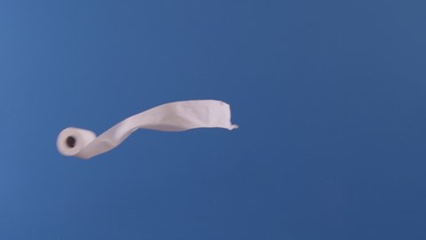 A toilet paper roll is seen flying across a blue screen in slow motion.