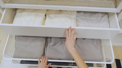 Pov shot of female shutting drawers with neatly organized clothes. Close up of woman hands closing shelves with outfits in wardrobe. Housewife using drawer with clothes in closet
