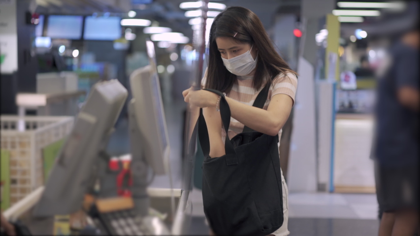 Young Asian woman in medical mask go grocery shopping, at supermarket cashier register counter, stocking up on foods, lifestyle during covid19 corona virus, say no to plastic bag, getting foods supply Royalty-Free Stock Footage #1051861063