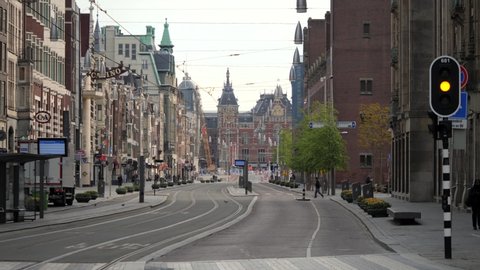 AMSTERDAM – MAY 03, 2020: Almost empty (few people) on the Damrak street in Amsterdam during a partial lockdown due to COVID-19 (Coronavirus). View from Dam Square on Central Station.