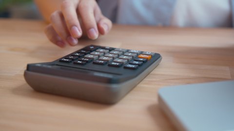 Close up shot of businesswoman or female accountant hand using a calculator doing the math calculating expenses, tax, analysis financial data working form home. Business and Financial Concept.