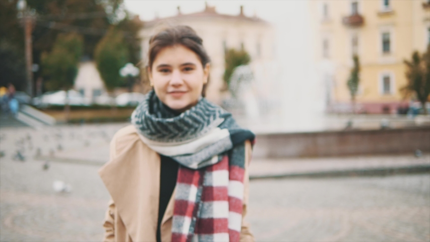Adorable girl is showing her thumb fingers up in the square, full of pigeons. Blured background, focus is on thumbs. Slow motion. Copy space. 4K.
