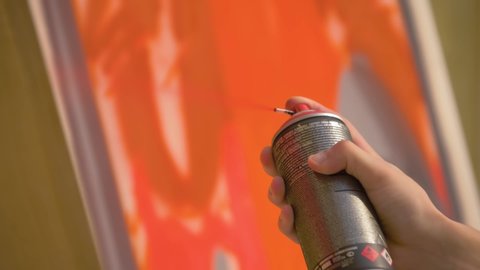 Super slow motion: man hand holding aerosol spray and painting colorful graffiti on wooden surface at summer street art festival: close up. Urban culture, outdoor activity, freedom, creativity concept
