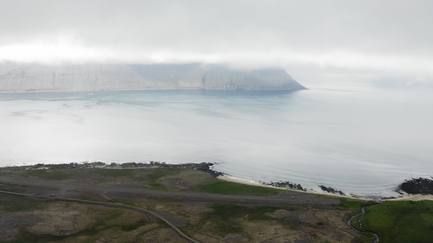 Aerial drone shot flying above beautiful Icelandic landscape. Top view from sky over majestic coastline, Atlantic ocean, mountains, road and sandy beach. Adventurous holidays in Westfjords, Iceland