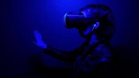 Girl wearing virtual reality glasses touches the air with her finger and gets a new virtual experience. Blue light.