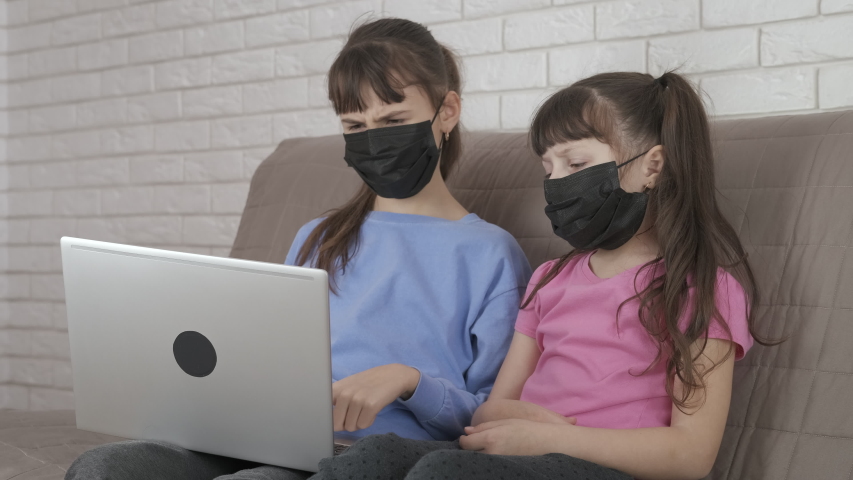 Children quarantined in the computer. Little masked sisters behind a laptop.