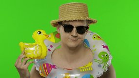 Shirtless young upset and exhausted man tourist with swimming ring and inflatable duck toy. Portrait of blonde guy in hat isolated on chroma key background. Green screen. Place for your logo or text - Powered by Shutterstock - Get 15% off with code: PIKWIZARD15