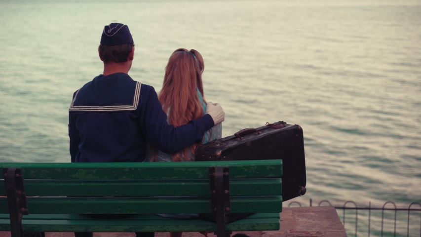 A young guy in uniform and a young girl are sitting on a bench and looking at the sea. 4k