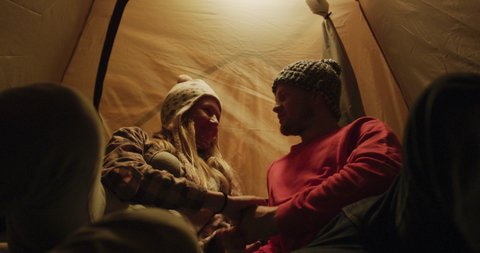 Caucasian couple having a good time on a trip to the mountains, lying in a tent at night in warm clothes, the man kissing the woman on the forehead, in slow motion