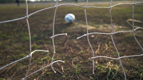 Kyiv, UKRAINE - January 2, 2020: Close-up of a torn soccer net. Soccer ball through the net. Old gate soccer field. Street sport. Child Game. The sun shines through the grid. The crisis. Football