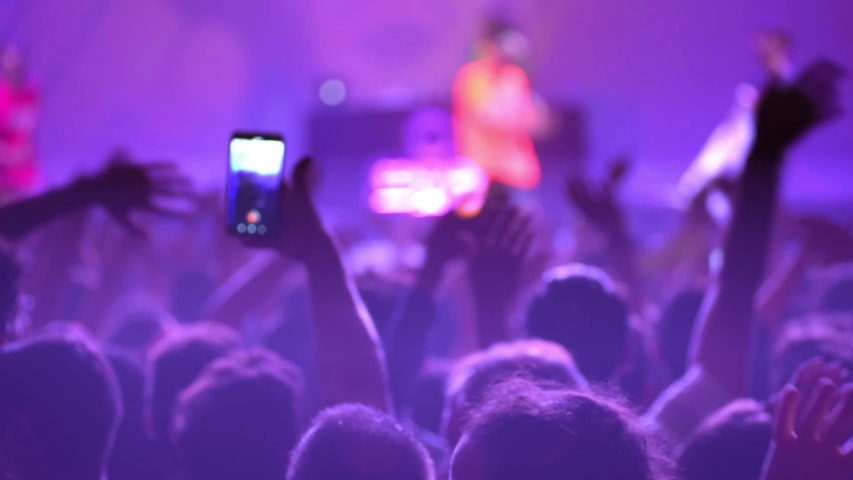 Happy people are watching an amazing musical concert. Merry fans jump and raise their hands up. Crowd of excited fans applauding to popular band performing favorite song. A group of fans with phones Royalty-Free Stock Footage #1051914112